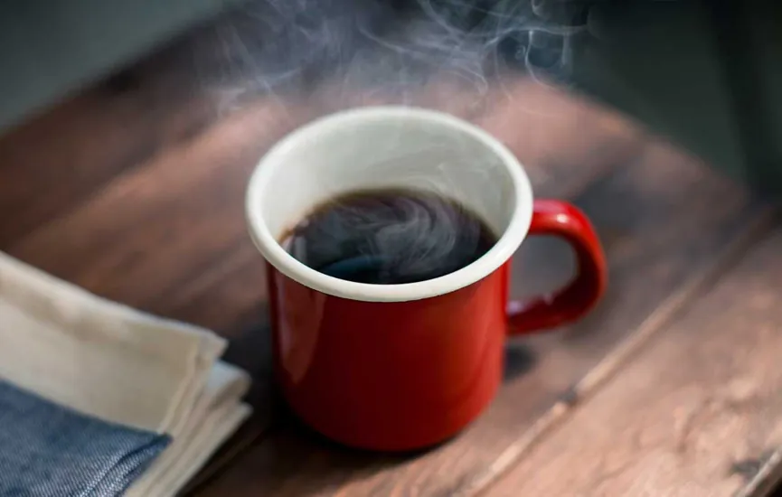 Модон ширээн дээр хар кофе бүхий улаан өнгийн сэнжтэй аяганаас уур савсан буй